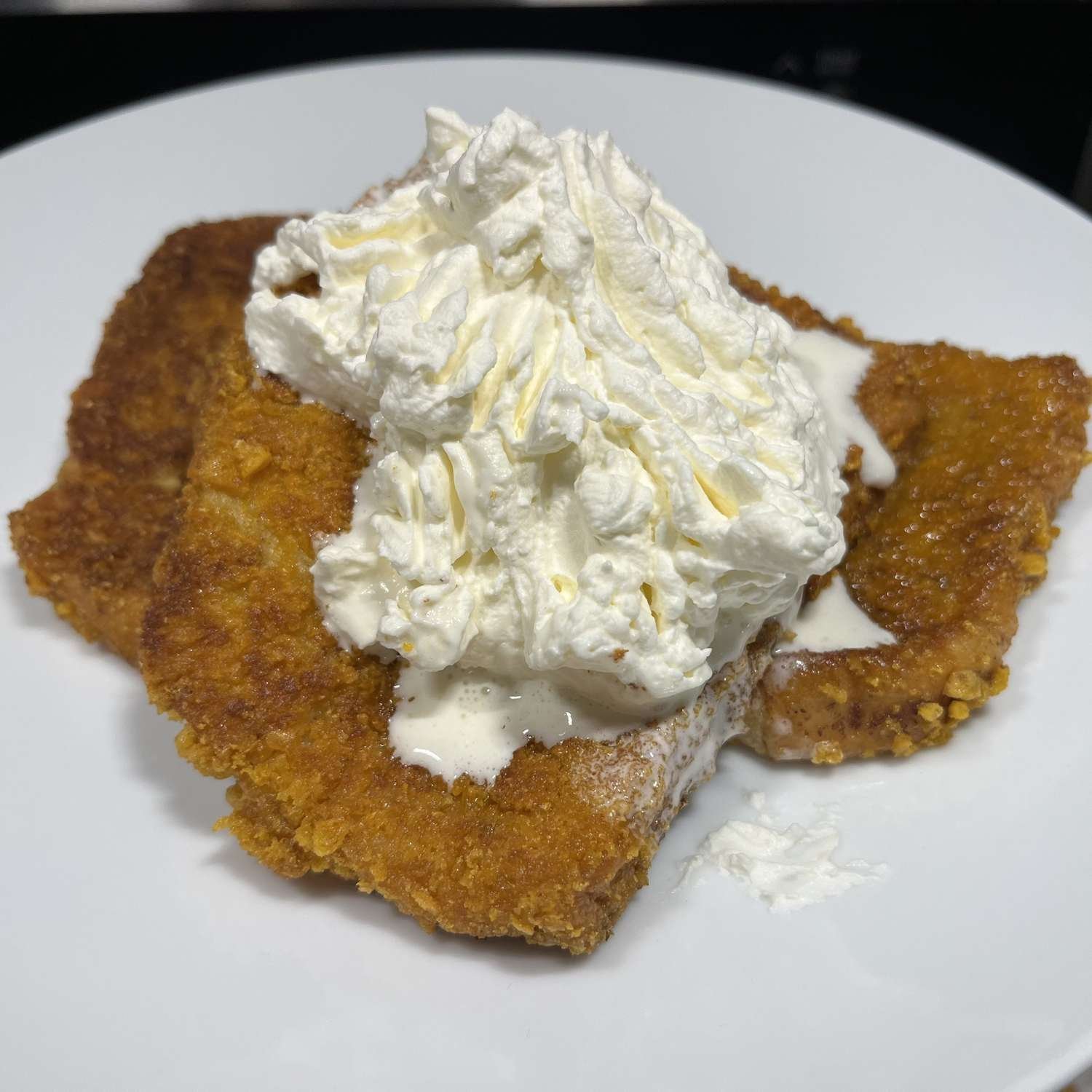 Two slices of golden brown French toast topped with a mountain of whipped cream