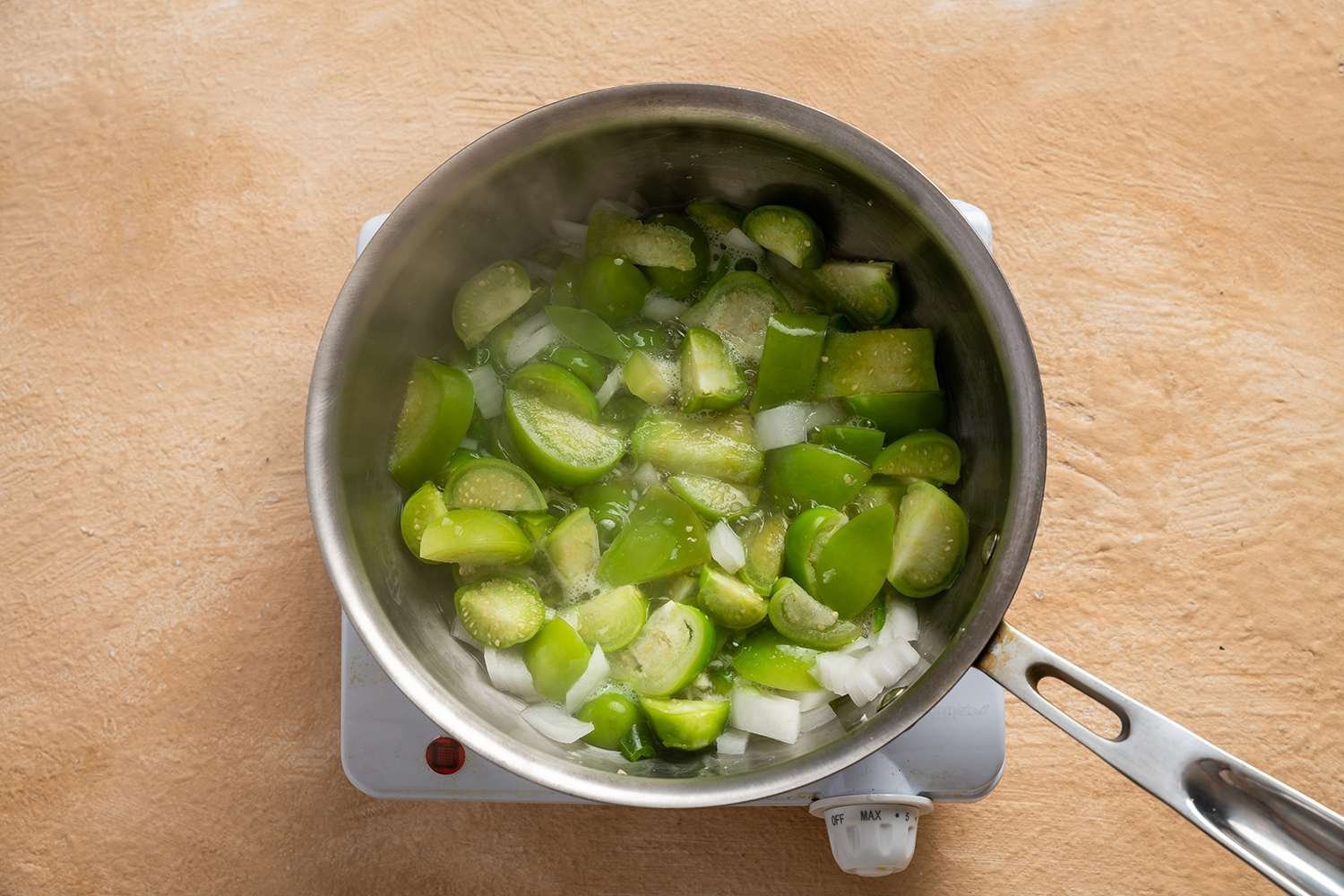 Tomatillos, onion, garlic, jalapeño, and water in a pot on a burner 