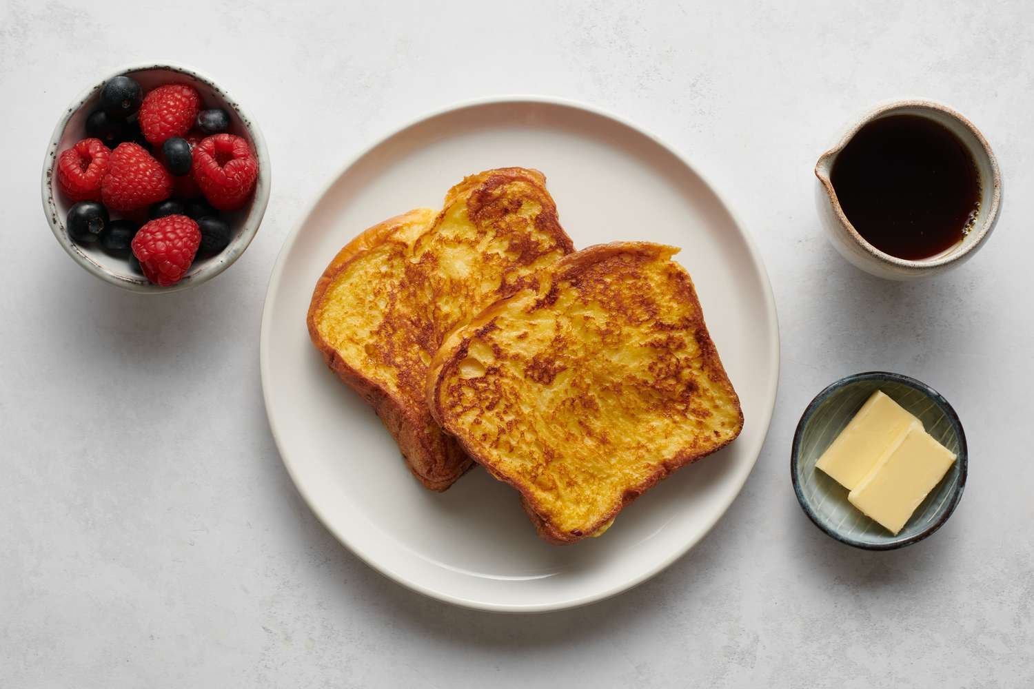 Un plato de tostadas francesas servidas con mantequilla, jarabe y bayas