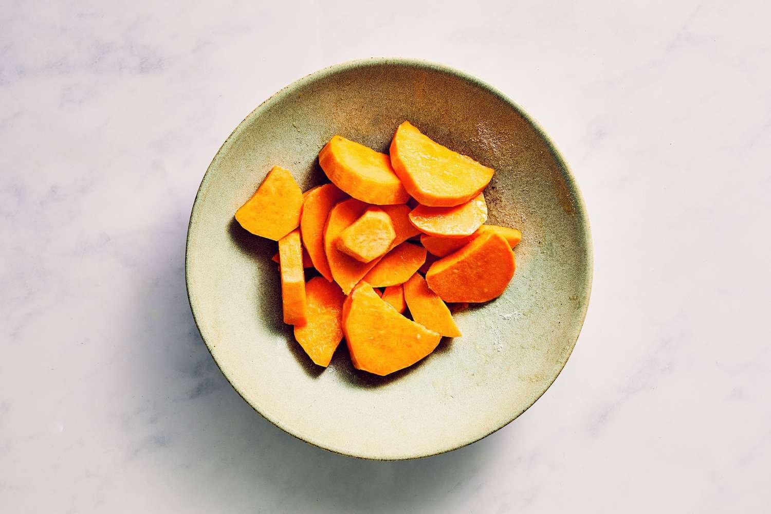 Un tazón de rodajas de batata mezcladas en aceite y sazonadas con sal