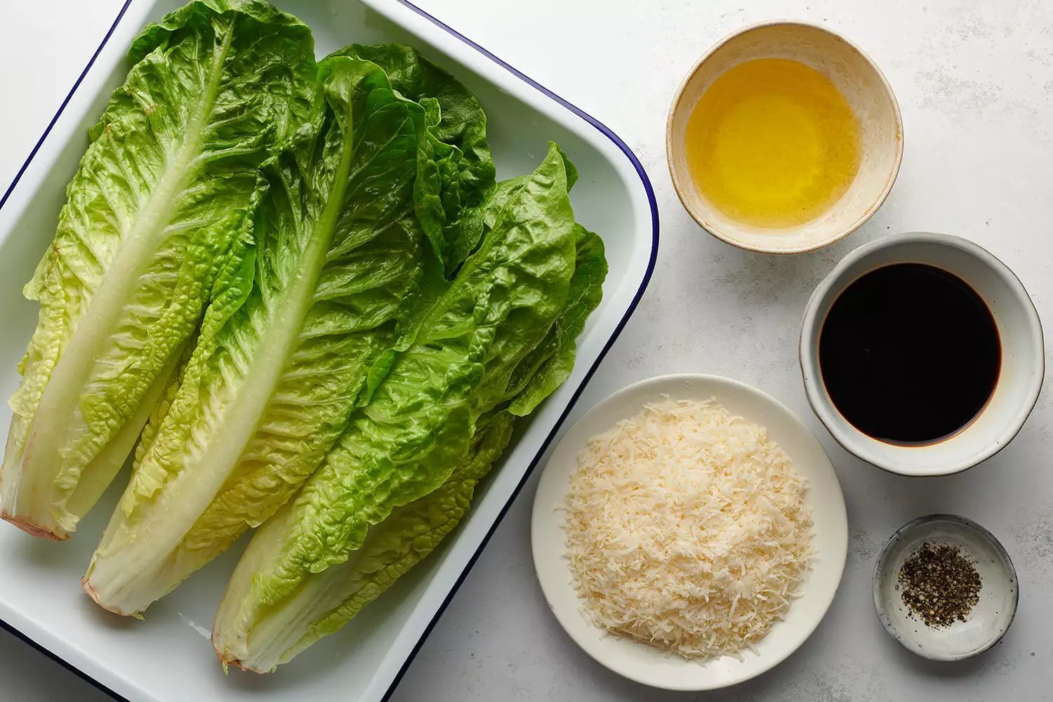 Alface romaine fresca, azeite, queijo parmesão e pimenta em uma mesa.