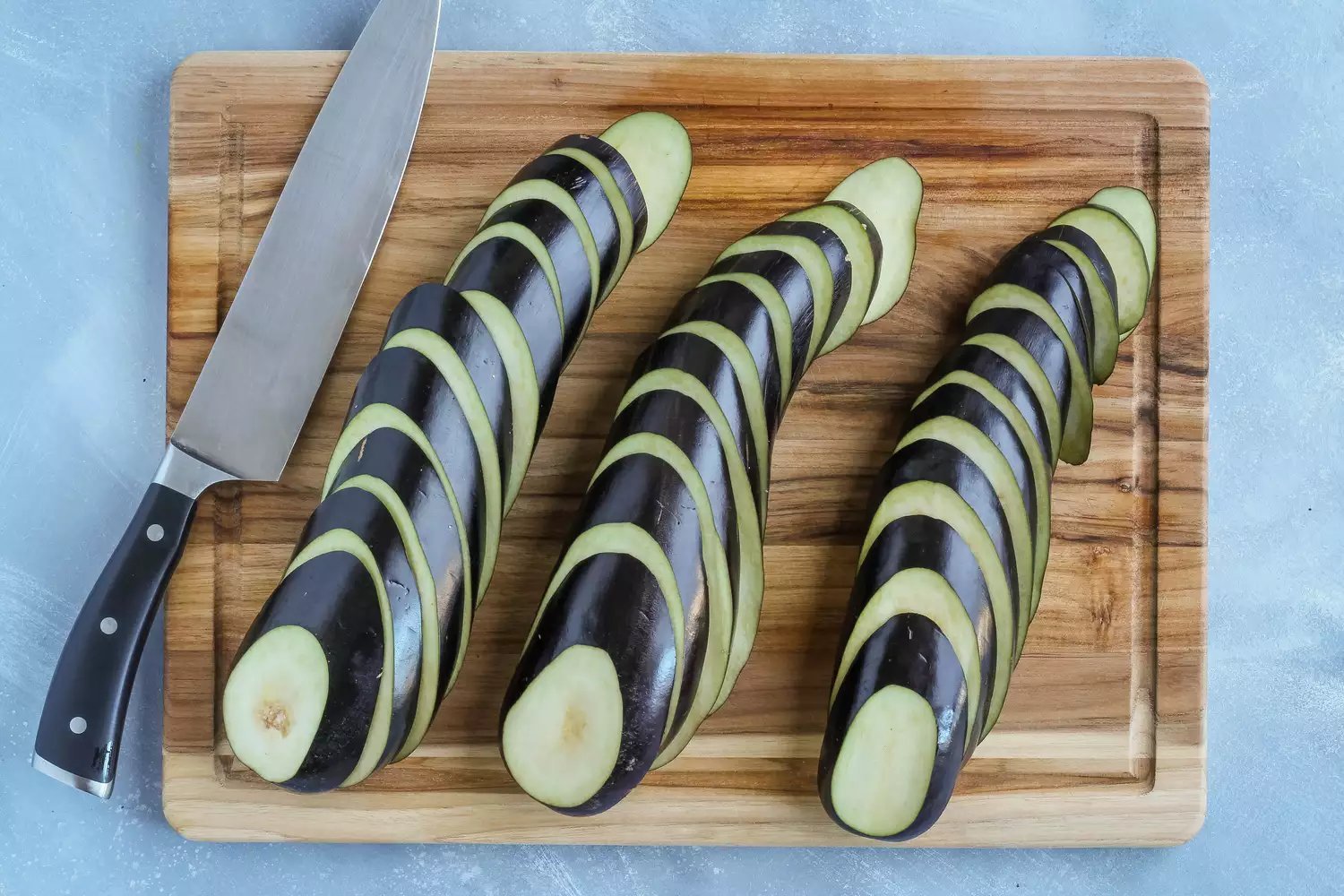 Berinjela cortada em fatias de 3/4 de polegada dispostas em uma tábua de corte de madeira