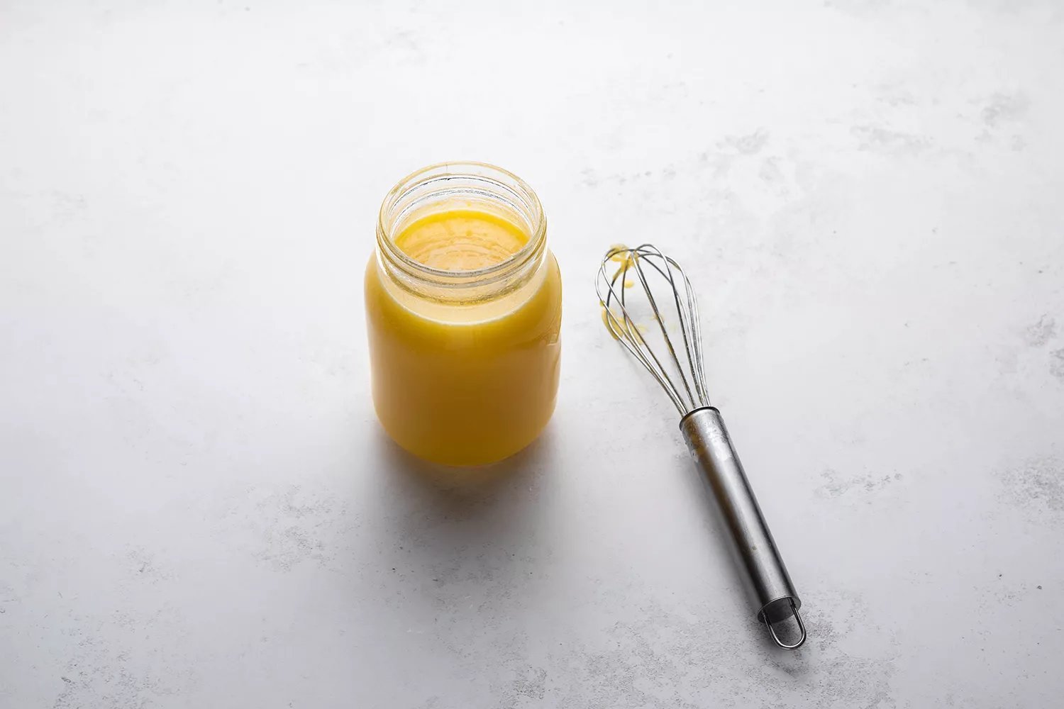 Lemon curd em um recipiente de vidro, ao lado de um batedor 