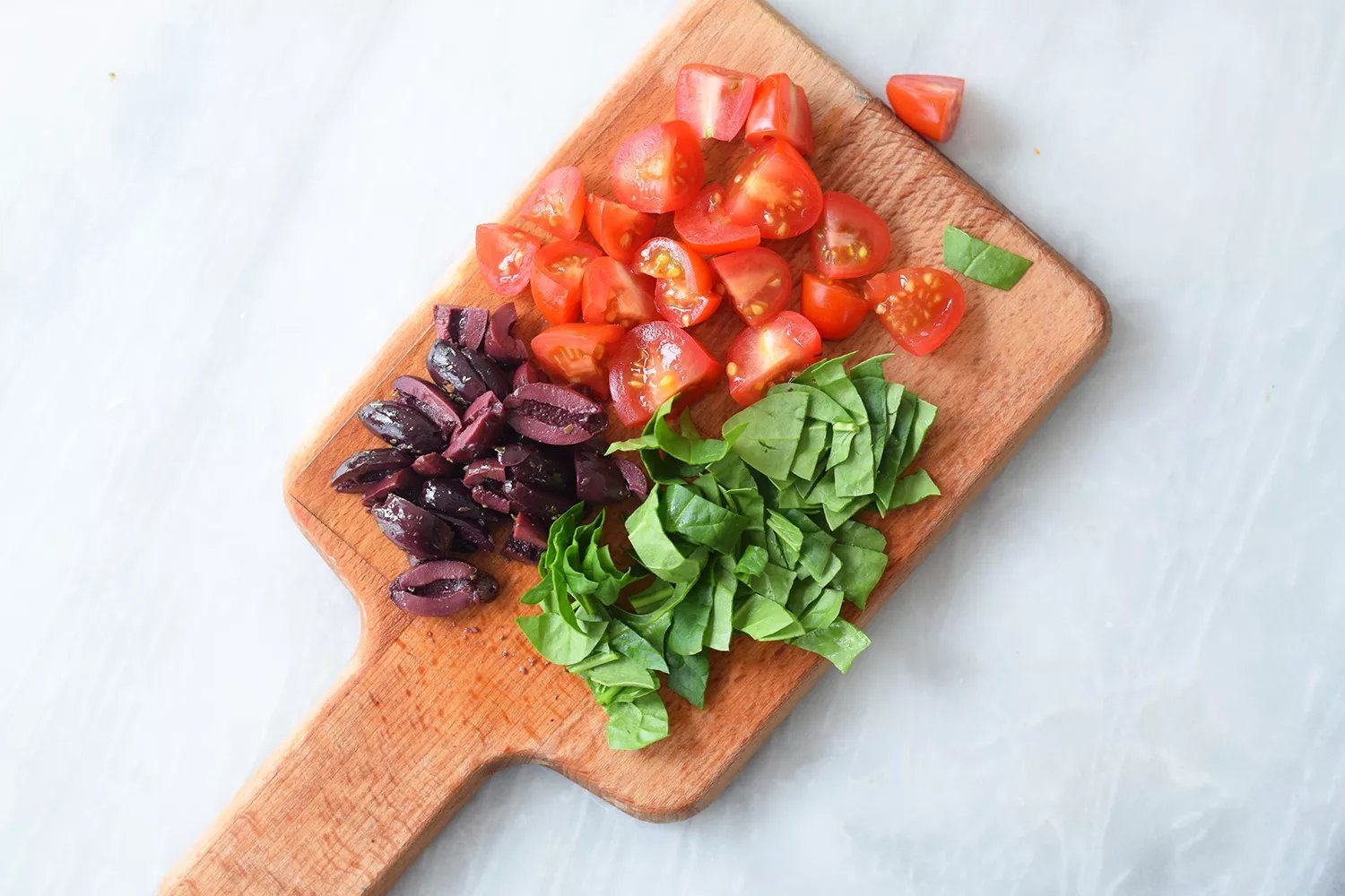 Tomates, espinafre e azeitonas picados em uma tábua de corte