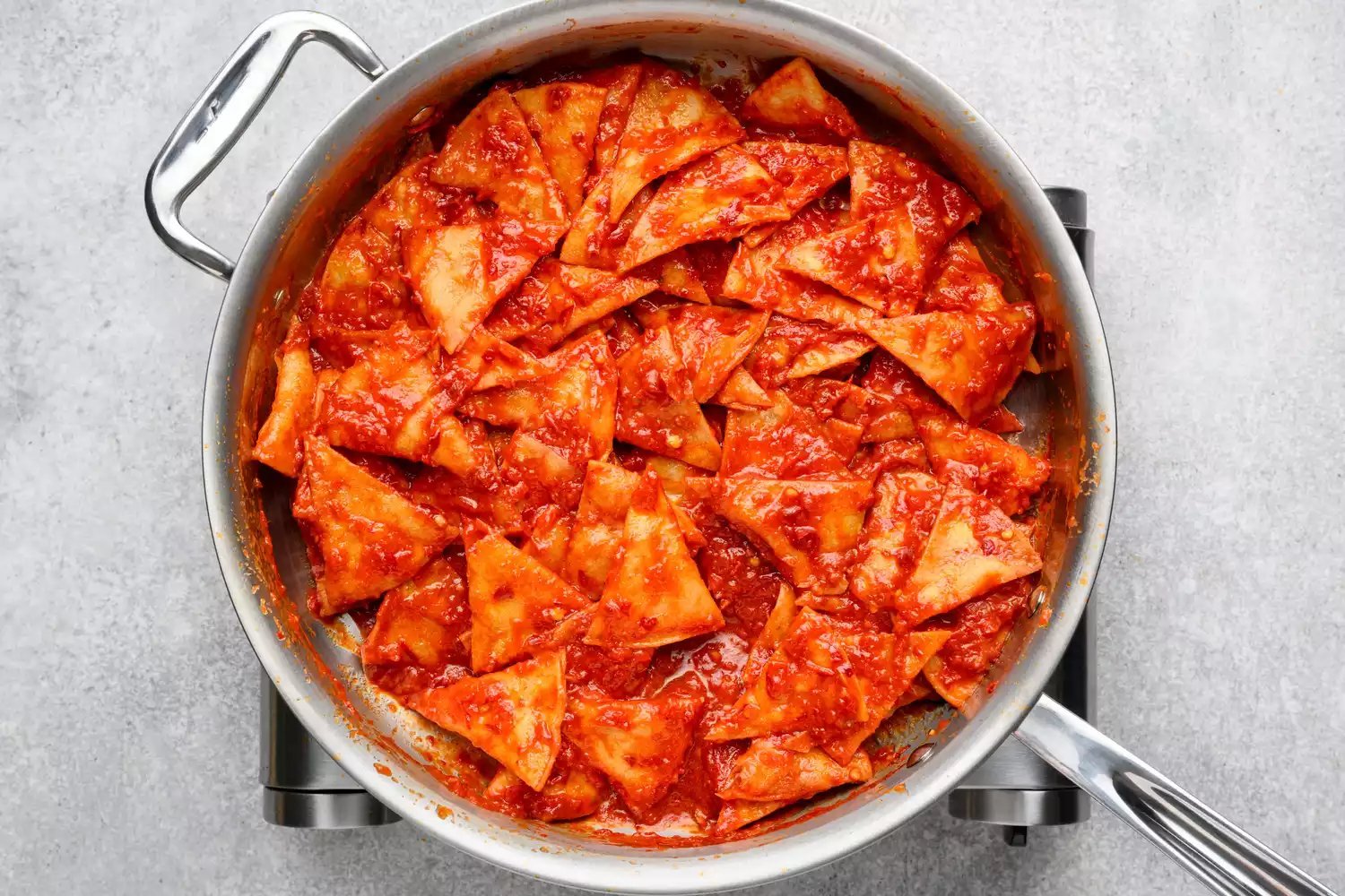 Uma panela de chips de tortilla fritos misturados em um molho de tomate e chile