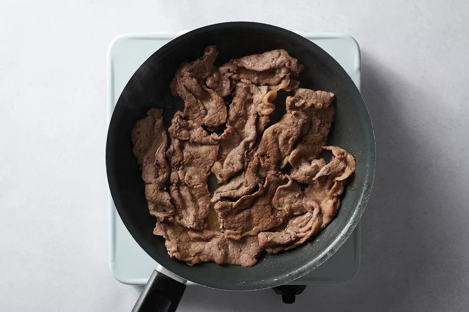 carne fatiada cozinhando na frigideira