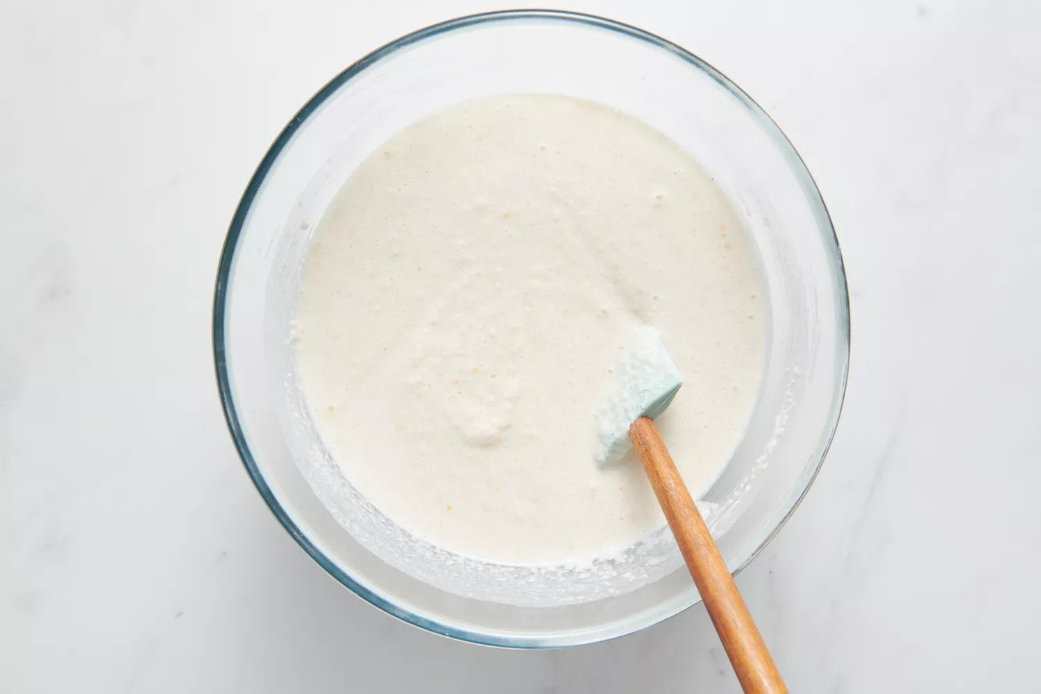 Uma tigela grande com uma espátula de silicone dobrando a massa de arroz Sona Masuri na massa de urad dal-feno-grego