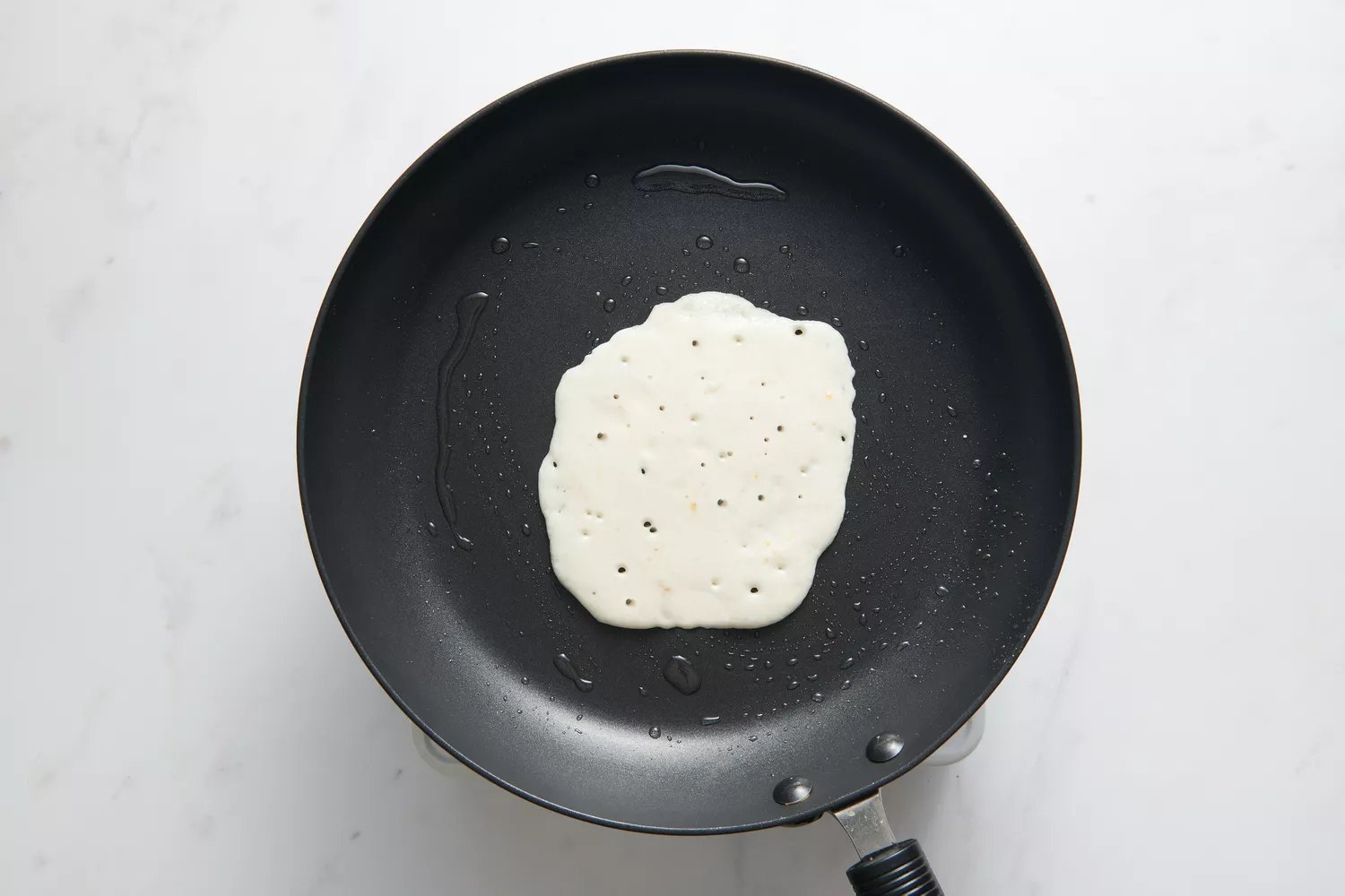 Uma pequena porção da massa derramada no meio da frigideira antiaderente untada