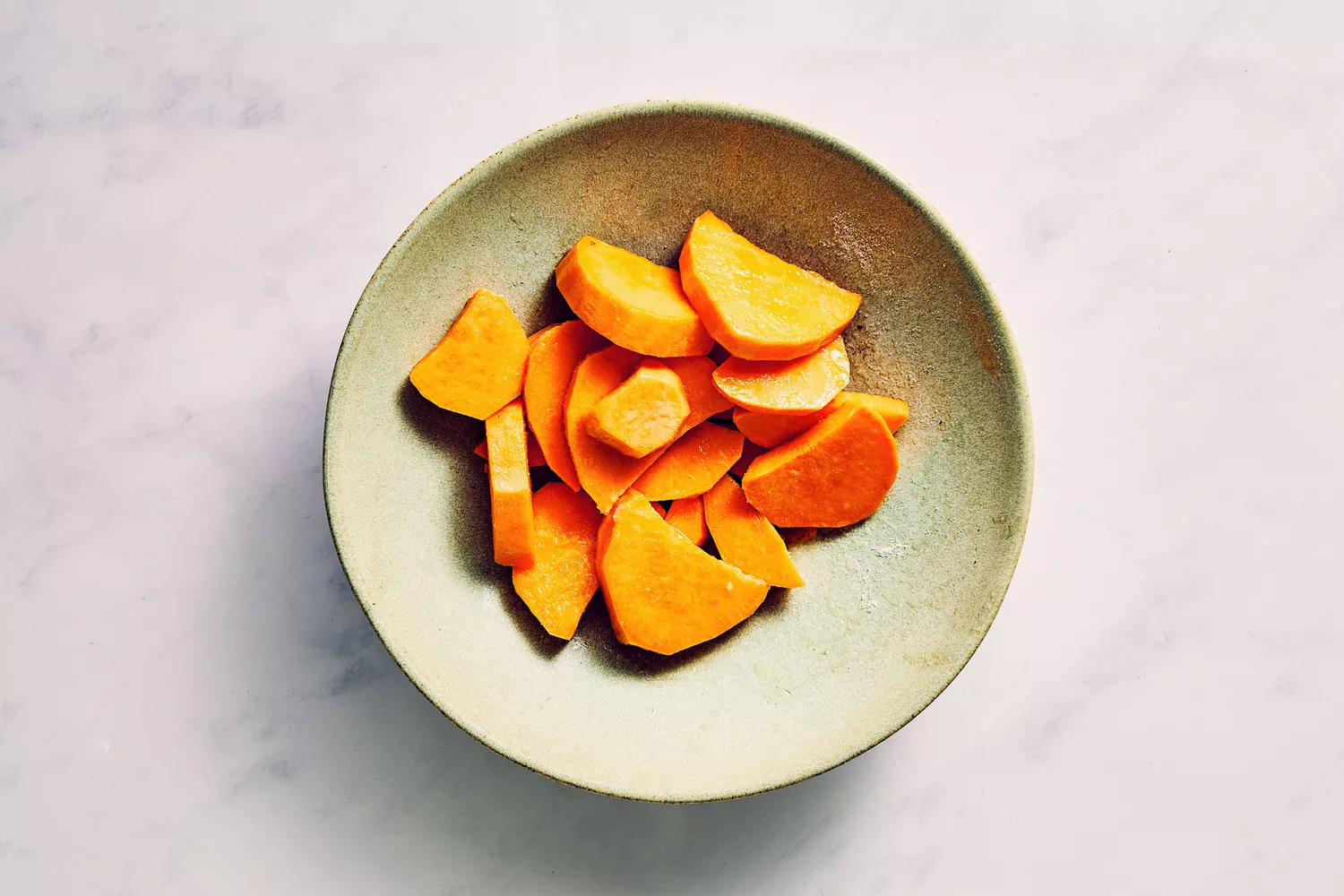 Uma tigela de batata-doce fatiada em óleo e temperada com sal