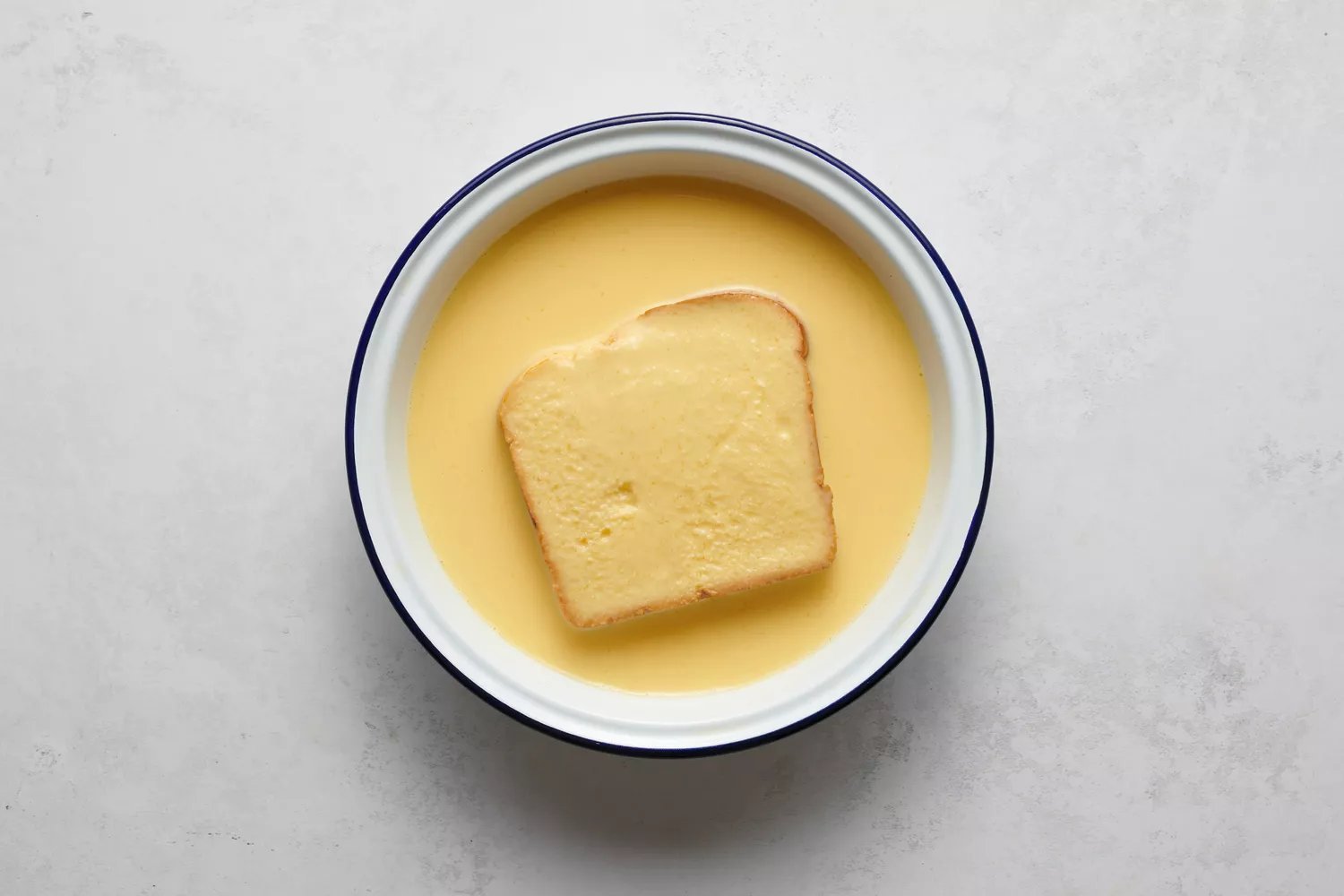 Um pedaço de pão mergulhando na mistura de ovos e leite batidos